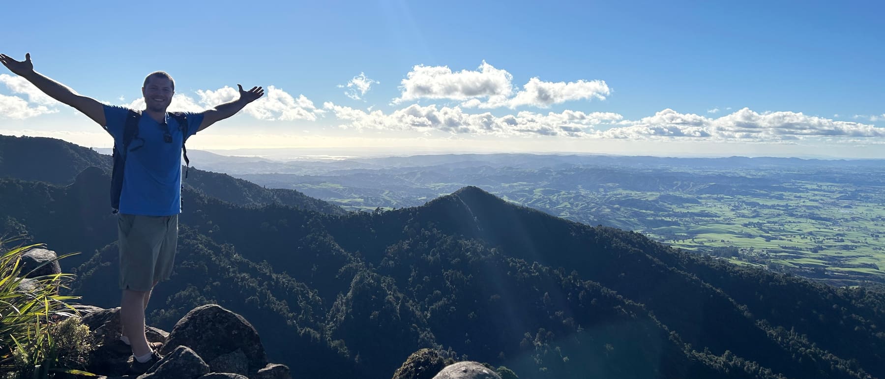 Thibaut Holl, founder of Salty Marketing, on a New Zealand summit, arms wide, with farmland stretching to the horizon